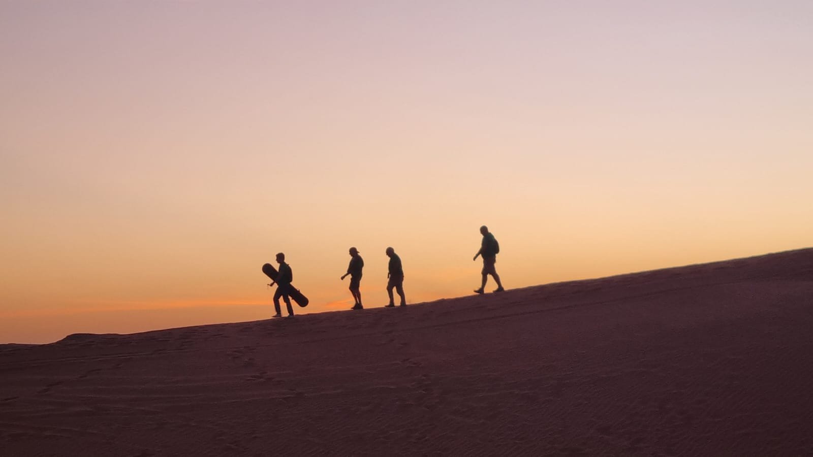 Djanet Tassili tour: silhouettes of trekkers crossing a dune crest at sunset in the Algerian Sahara