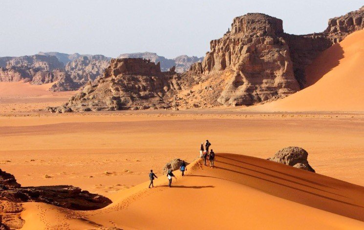 Djanet Tassili tour: travellers walking a dune crest below the Tassili plateau