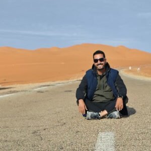 Taghit desert tour: empty Saharan road with high orange dunes rising behind, Algeria